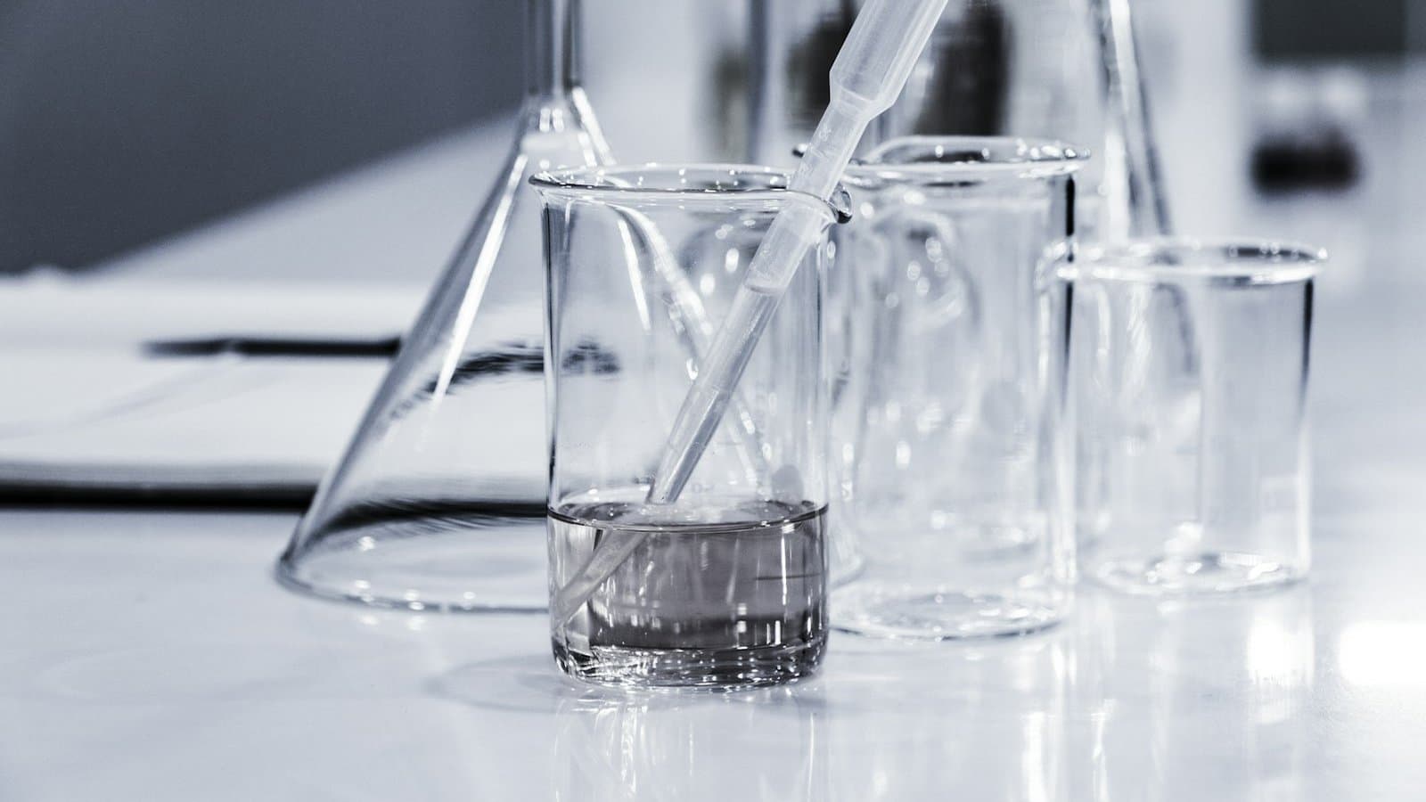 Three clear glass beakers on a laboratory tabletop, the glassware used in water quality analysis for industrial monitoring programmes