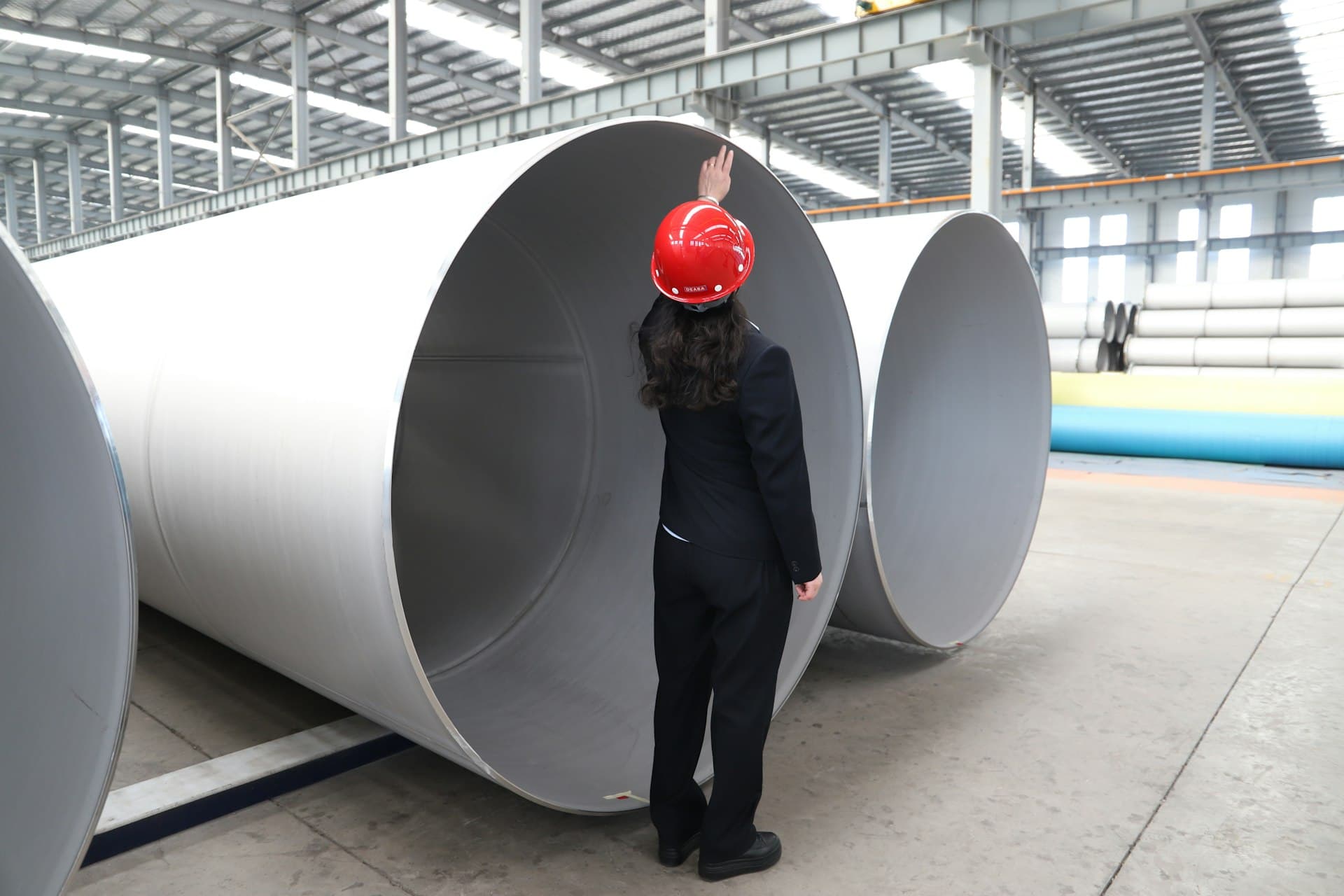 Worker inspecting large-diameter water pipes in a fabrication hall — risk lives in the details