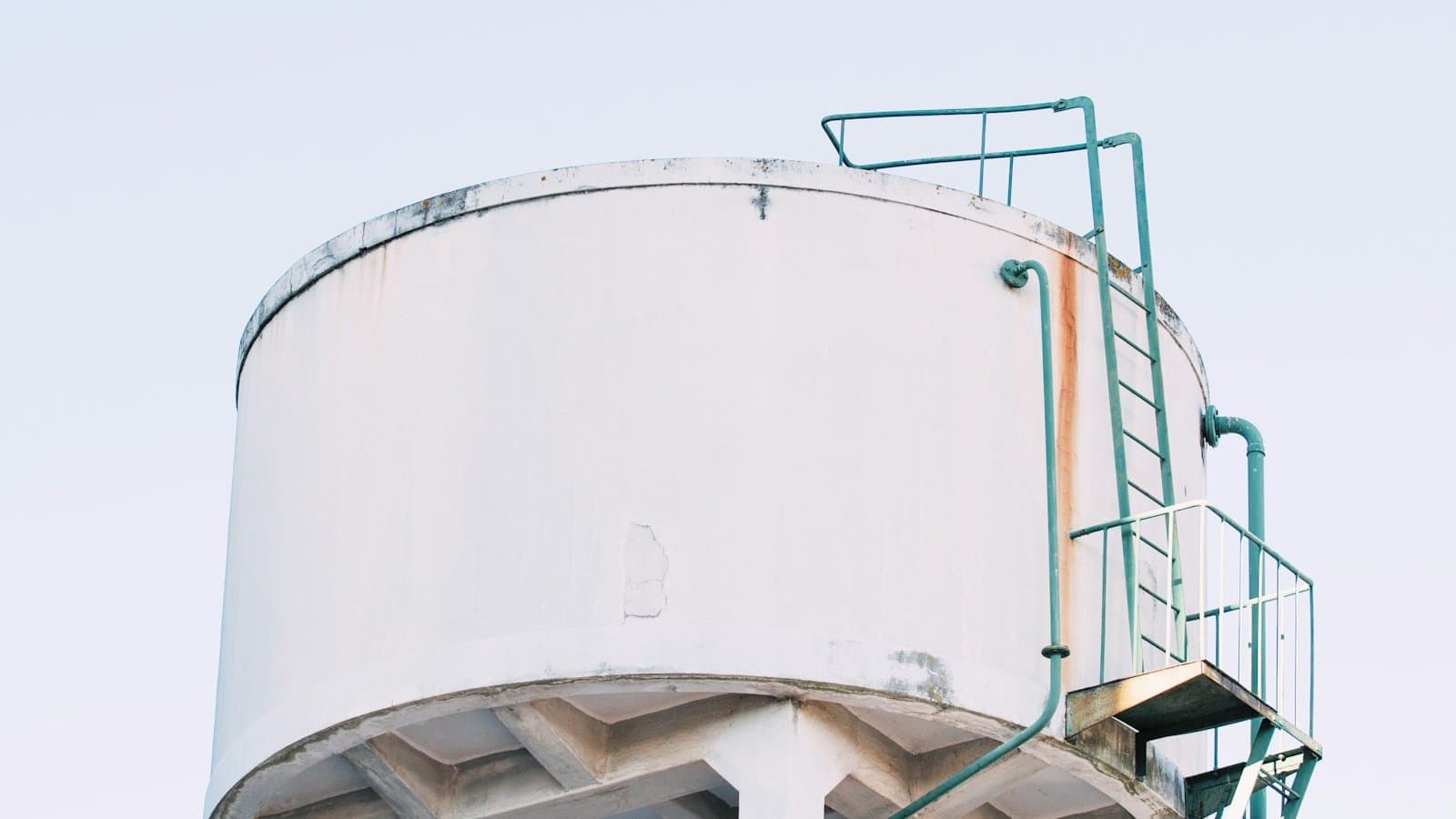 Large round white concrete industrial water storage tank with green metal access ladder at an industrial facility