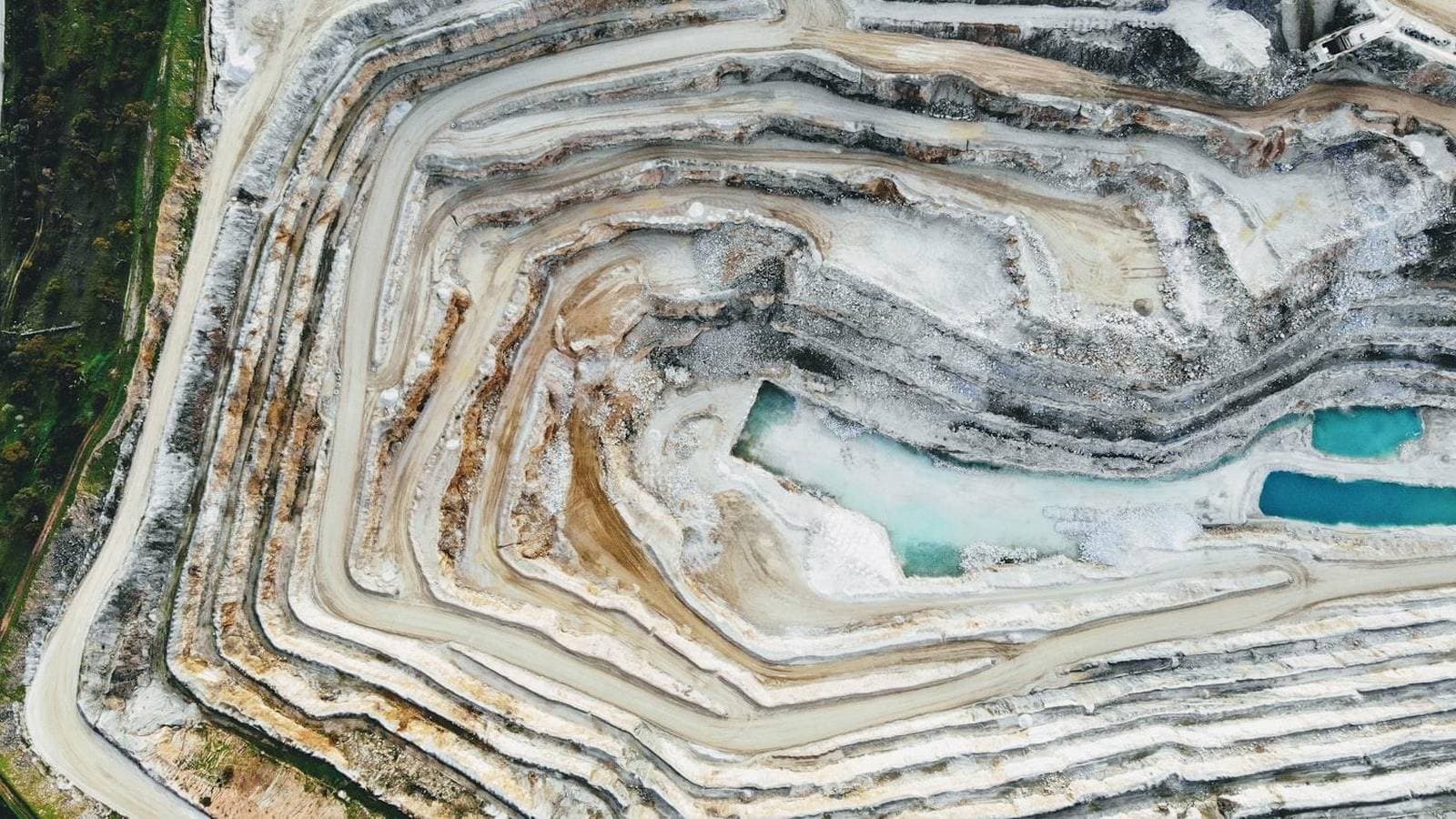 Aerial view of a mining quarry with a turquoise acid drainage pool, the visual signature of acid mine drainage and the water treatment challenge at every extraction site