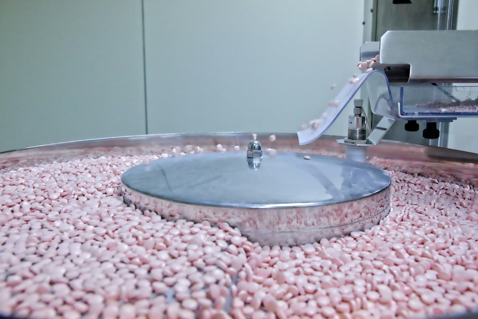 Pink pharmaceutical tablets moving through a production machine at a drug-manufacturing plant