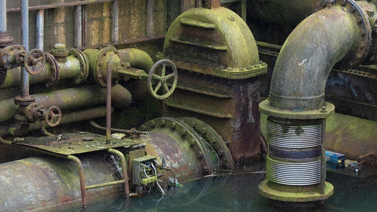 Industrial pipes and water infrastructure at a wastewater treatment facility, representing the solids-handling systems central to sludge dewatering operations