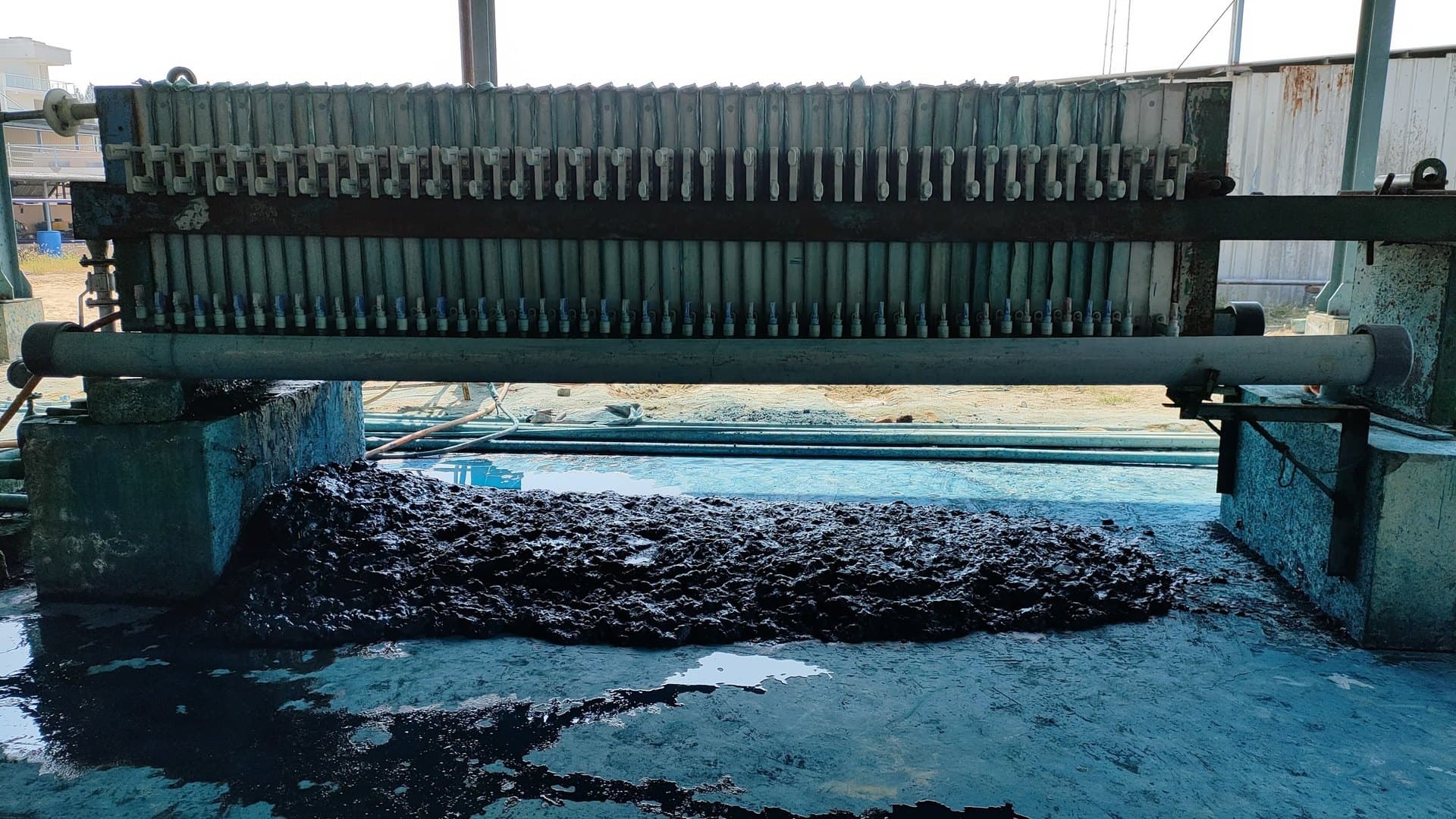 Filter press dewatering dye-laden textile sludge at an effluent treatment plant, with pressed cake dropping to the collection bay