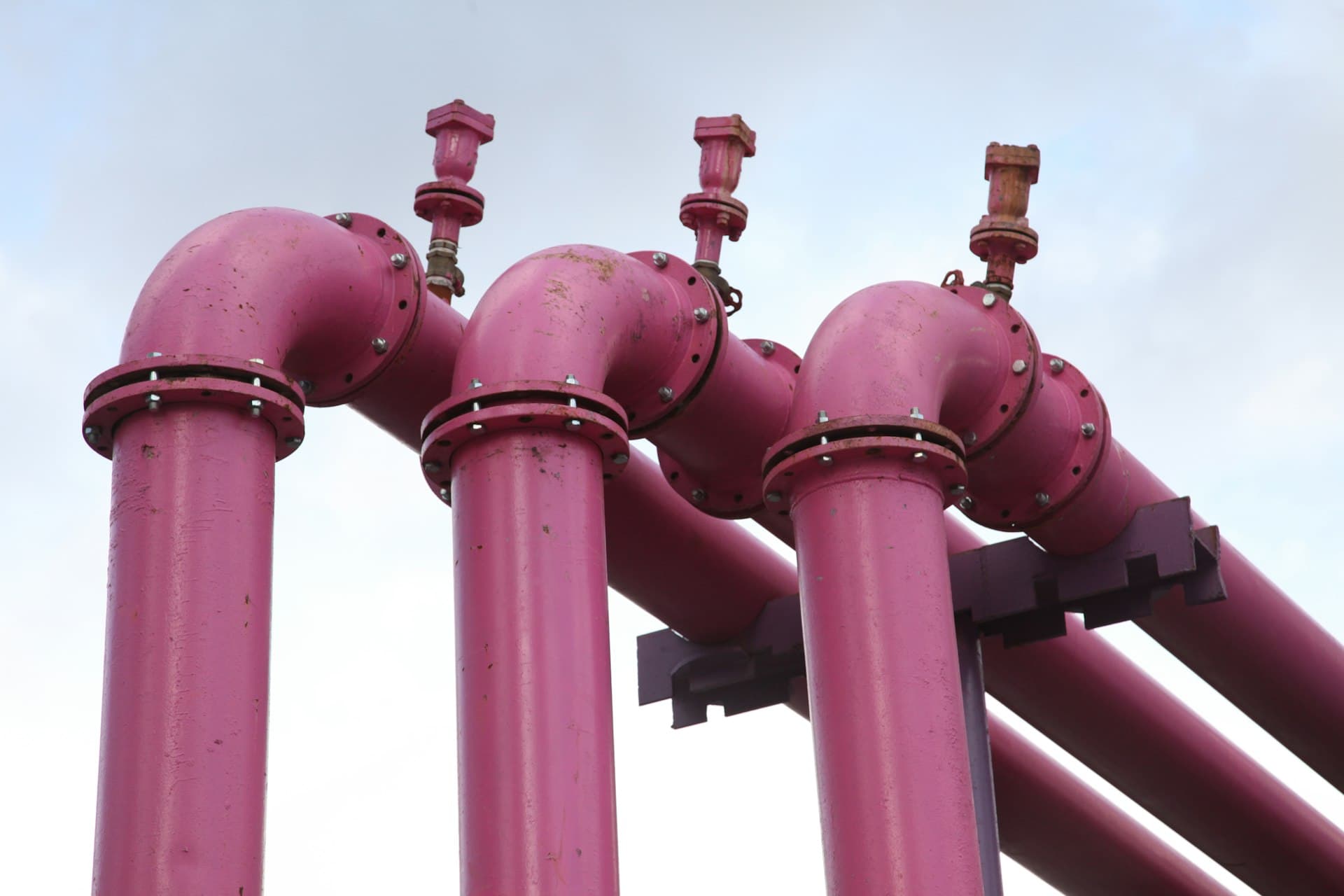 Looping pink pipelines outside a factory — water routed round and round instead of once through